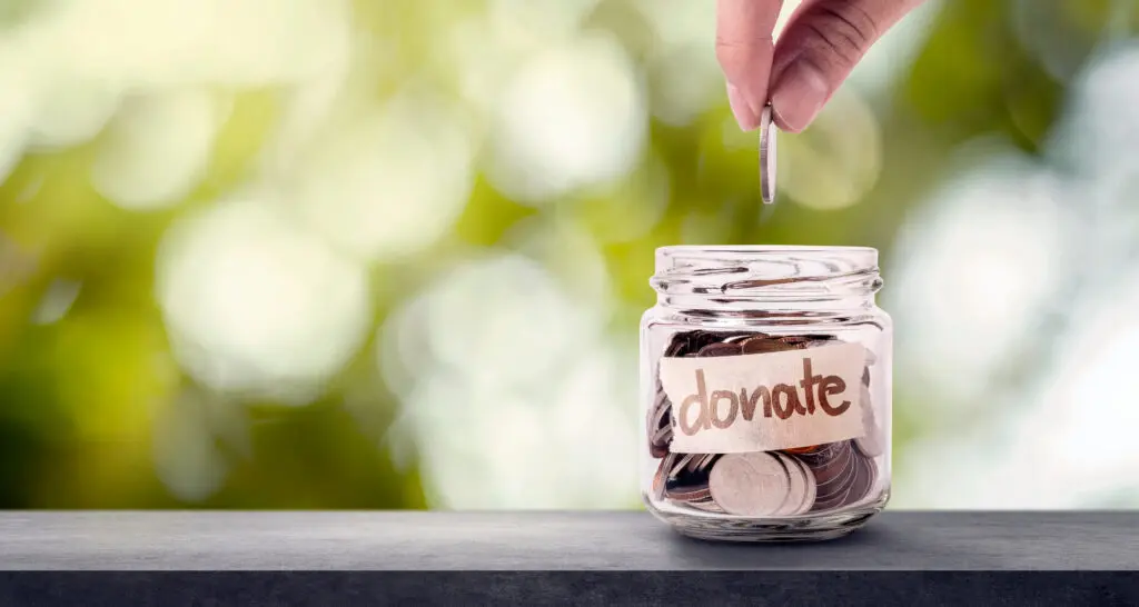 Hand putting coins in glass and have words donate write on label. Giving and donation concept.